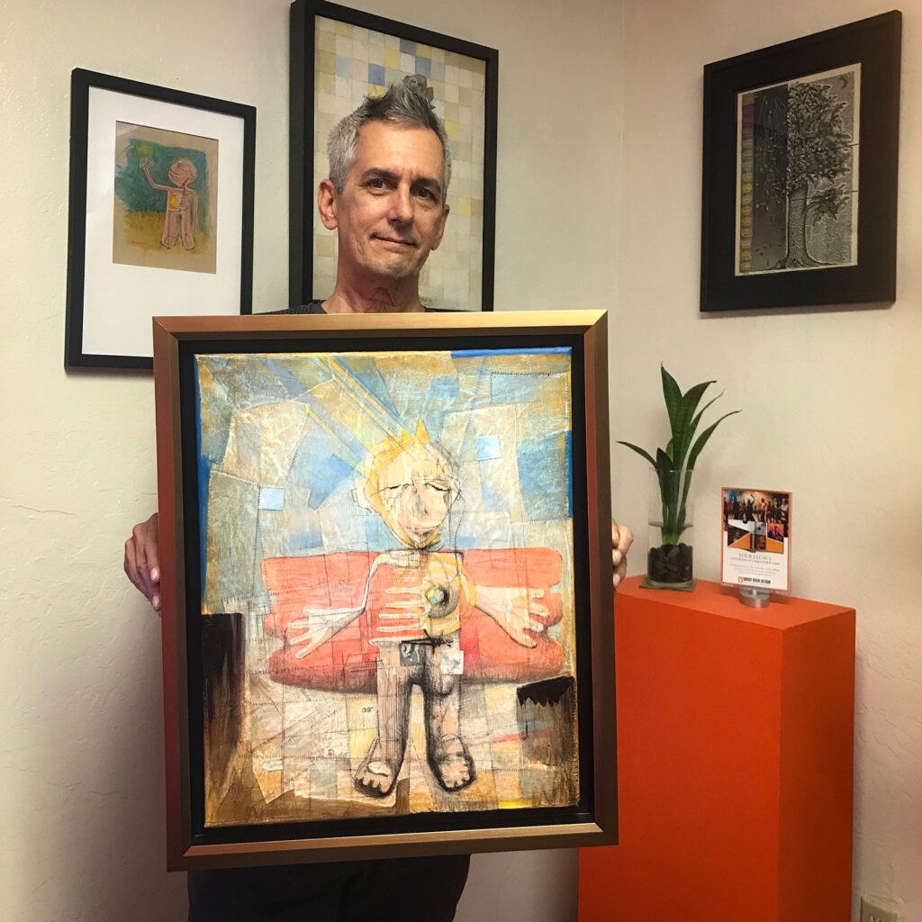 David holding one of his framed pieces, "Little Hero"